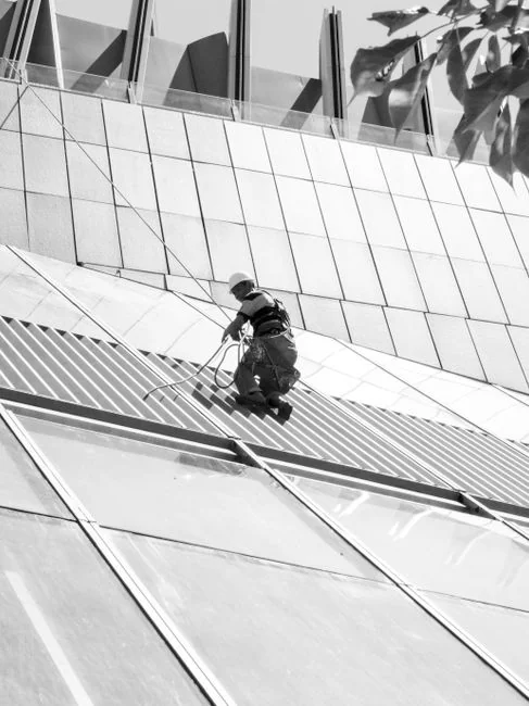our-story Two workers cleaning windows on a glass building facade using a lift platform, enhancing building aesthetics.